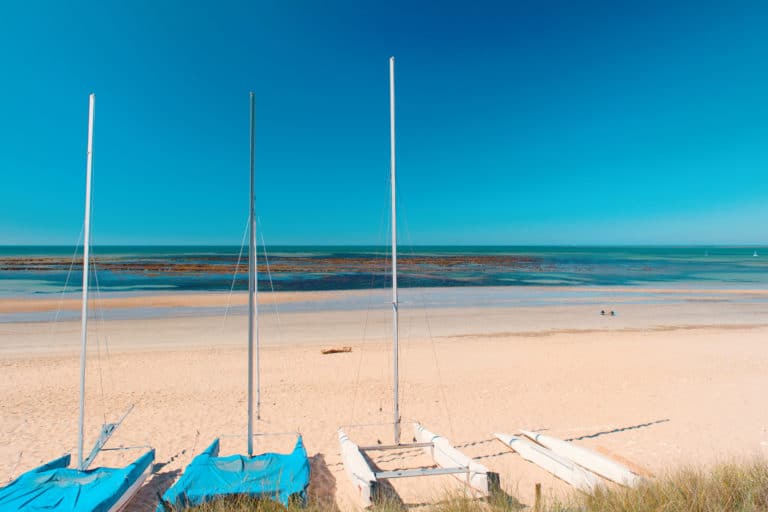 Voiliers sur plage de sable, mer turquoise à l'horizon.