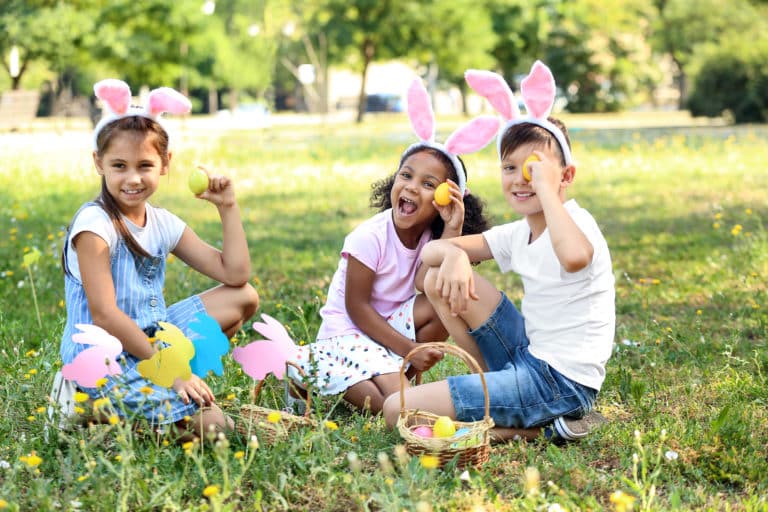 Enfants avec oreilles lapin chassent œufs en plein air.